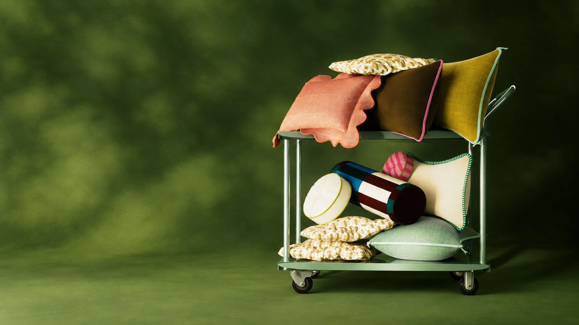 Colorful pillows piled on a mint-green trolley against a soft green backdrop — Home, 3D campaign for the Home & Living universe